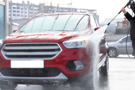 washing car at autowash. Car wash. red machine under the pressure of water at a car wash. car in foam. woman washing carの写真素材
