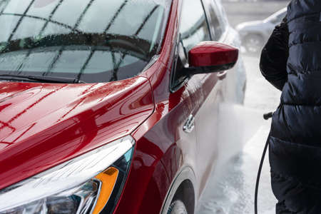 washing car at autowash. Car wash. red machine under the pressure of water at a car wash. car in foam. woman washing carの写真素材