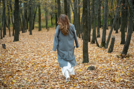 girl in a coat in the autumn forest. redhead woman walking in the park. white boots. Close portrait of beautiful womanの写真素材