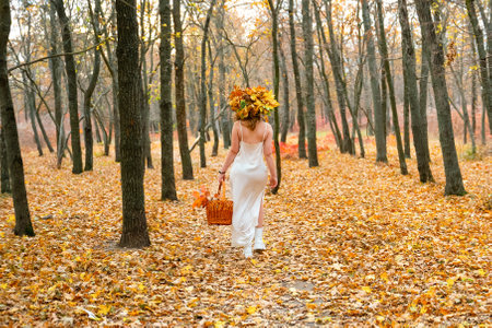 portrait of young red-haired woman in autumn forest. girl in a long white dress with basket. Beautiful women's body in silk nightwear. nymph.wreath of flowersの写真素材