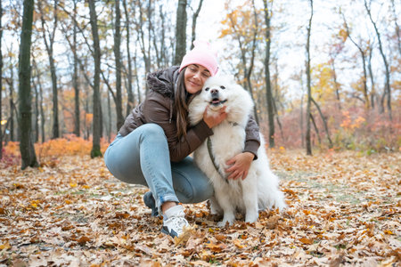 beautiful smiling girl with  Samoyed dog in the autumn park. brunette woman have fun with fluffy beautiful dog . girl is kissing her dogの写真素材