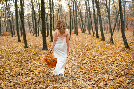 portrait of young red-haired woman in autumn forest. girl in a long white dress with basket. Beautiful women's body in silk nightwear. nymph.wreath of flowersの写真素材