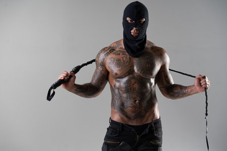 Muscular shirtless young man with whip in a mask. Men tattoo casual fashion. Portrait of a handsome male model. Muscular athletic sexy male witの写真素材