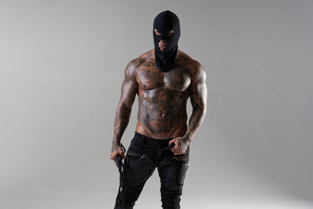 Muscular shirtless young man with whip in a mask. Men tattoo casual fashion. Portrait of a handsome male model. Muscular athletic sexy maleの写真素材