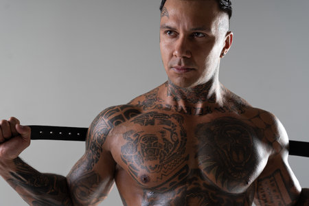 Muscular shirtless young man with whip in a mask. Men tattoo casual fashion. Portrait of a handsome male model. Muscular athletic sexy male witの写真素材