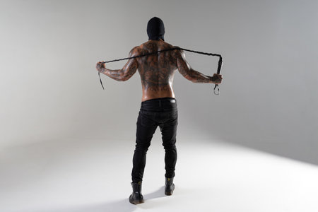 Muscular shirtless young man with whip in a mask. Men tattoo casual fashion. Portrait of a handsome male model. Muscular athletic sexy maleの写真素材