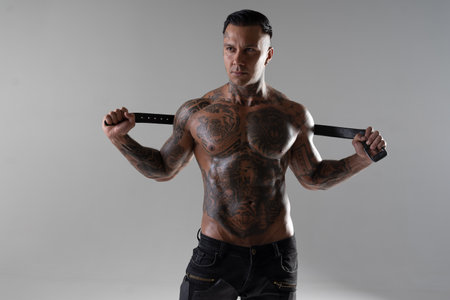 Muscular shirtless young man with whip in a mask. Men tattoo casual fashion. Portrait of a handsome male model. Muscular athletic sexy male witの写真素材