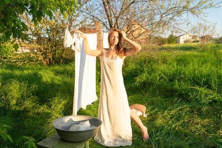 A young woman in a long white dress is washing clothes in the spring garden.の写真素材