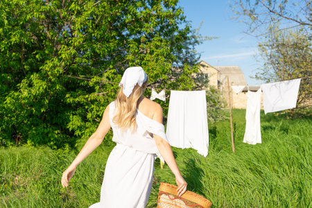 A young woman in a white dress and a hat stands in a field with clothes drying in the sunの写真素材