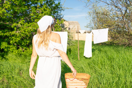 Young woman in white dress with a basket of clothes hanging on the clotheslineの写真素材