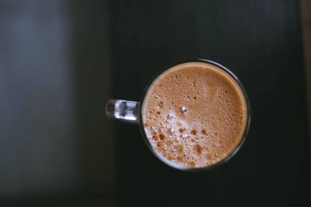 chocolate frothy coffee in a glass on the brown table