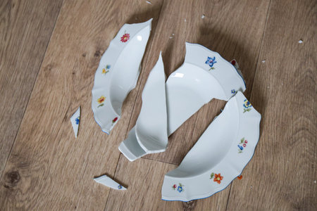 Shards of a broken plate on the wooden floor. Broken white ceramic plate on the wooden floor. Broken dishes. Top view.の写真素材
