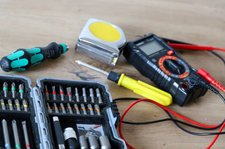 Variety drilling tools, screwdriver, measuring tape and digital multimeter on wooden background