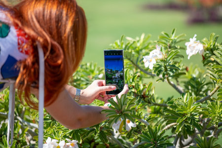 A red haired woman is making a picture of beautiful flowers with a smartphone