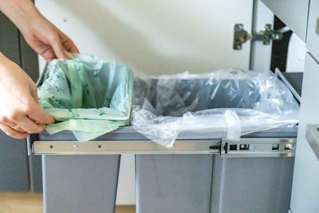 A housewife fodling a garbage bin in kitchen with a garbage bag. Waste separation concept