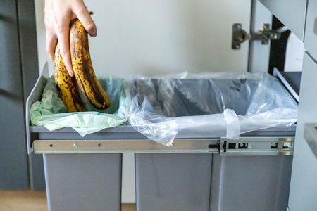 A housewife throwing tainted bananas into a garbage bin in kitchen. Waste separation concept