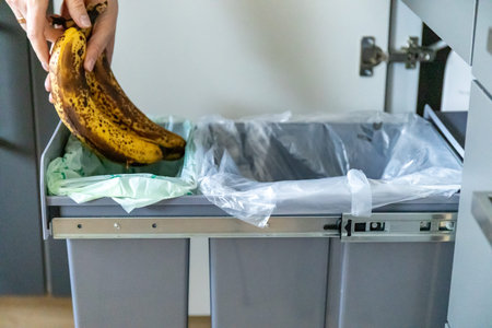 A housewife throwing tainted bananas into a garbage bin in kitchen. Waste separation concept