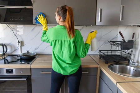 Young woman in bright green cloth cleaning kitchen table top