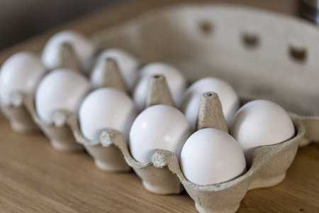 Open egg box with ten white eggs on wooden table. Fresh organic chicken eggs in carton pack or egg...