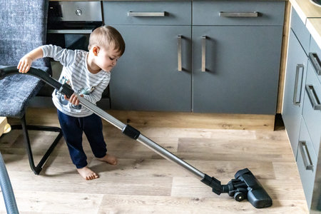 Little kid using vacuum cleaner at home, small boy cleaning floor in apartment, child doing housework having funの写真素材