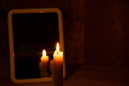 candle light in the reflection of a mirror standing on a table in a dark roomの写真素材