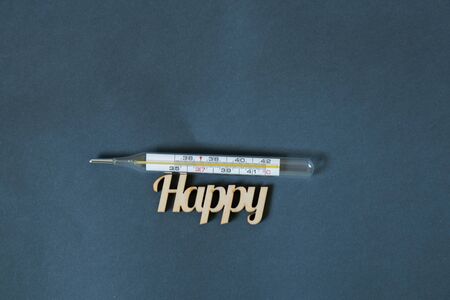 glass thermometer and the word happiness made of wood on a dark
