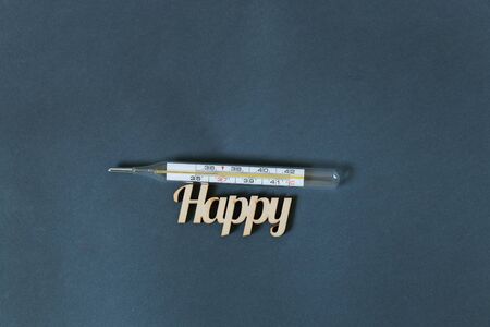 glass thermometer and the word happiness made of wood on a darkの写真素材