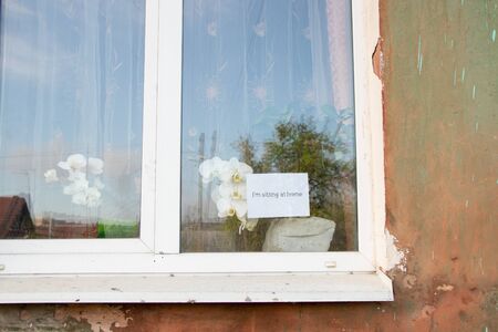 sitting at home the word in English written by hand hanging on a window of a house
