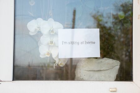 sitting at home the word in English written by hand hanging on a window of a houseの写真素材