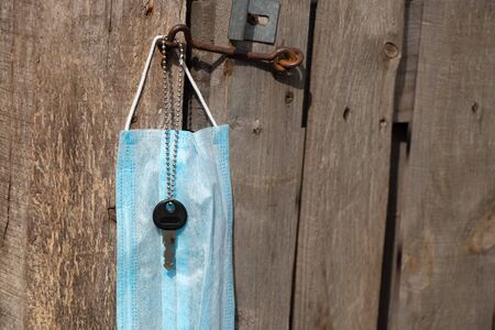 medical mask hanging on a hook and a door key on an old wooden gate in Ukraine on the street duringの写真素材
