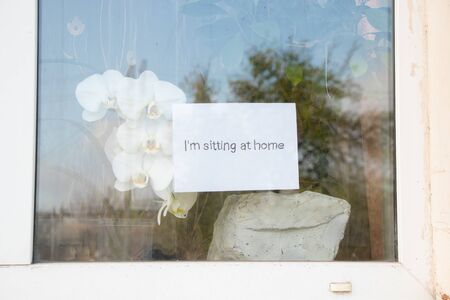 sitting at home the word in English written by hand hanging on a window of a houseの写真素材