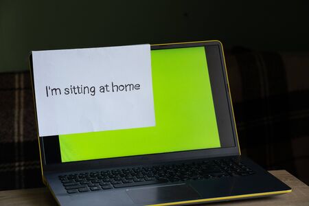 laptop with a green screen on a table in a room at home and a sheet with an inscription in English sitting at home in the period.の写真素材