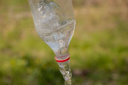 water is pouring from a plastic bottle on a blurred green background in the street duringの写真素材