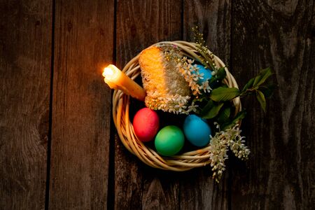 Easter dinner, colored chicken eggs and candle flame on an old wooden table in the evening