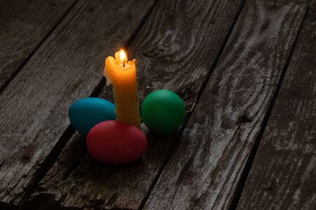 Easter dinner, colored chicken eggs and candle flame on an old wooden table in the eveningの写真素材