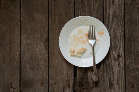 a white dirty plate with leftover food after lunch stands on an wooden boardの写真素材