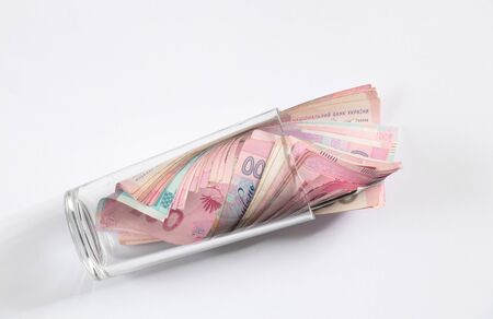 hryvnia and dollar lie in a glass cup on a white background