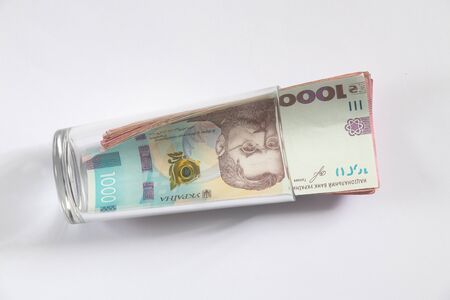 hryvnia and dollar lie in a glass cup on a white background