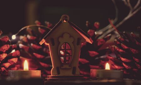 wooden house as a Christmas decor and a garland on a wooden table and candles, New Year