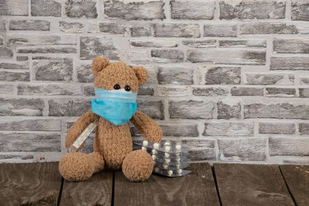 children's brown teddy bear with a thermometer tablets and a medical mask during the pandemic periodの写真素材