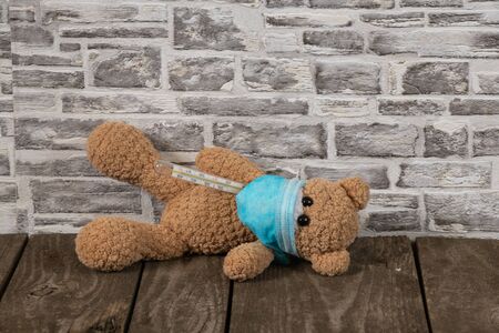 baby brown teddy bear with a thermometer and a medical mask during the pandemic periodの写真素材