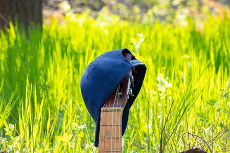 baseball blue cap hanging on an old guitar stands on a background of grass