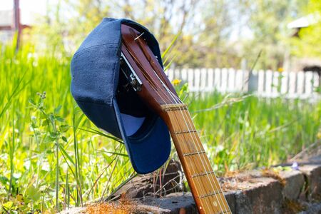 baseball blue cap hanging on an old guitar stands on a background of grassの写真素材