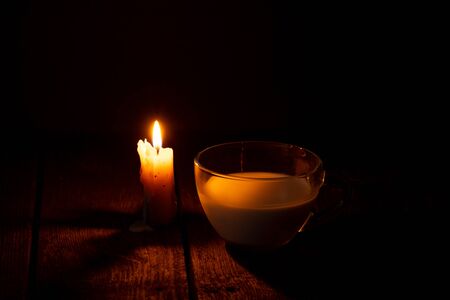 candle flame and cup with milk on a wooden table in a roomの写真素材
