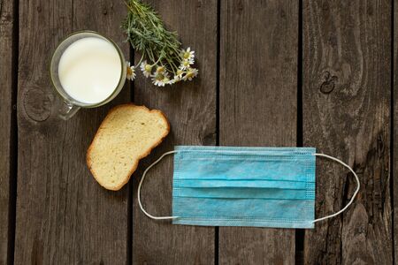 medical mask a piece of bread and a glass of milk on a wooden table at home