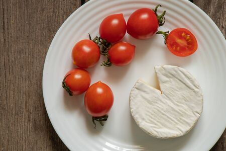 soft brie cheese and cherry tomatoes on a tableの写真素材