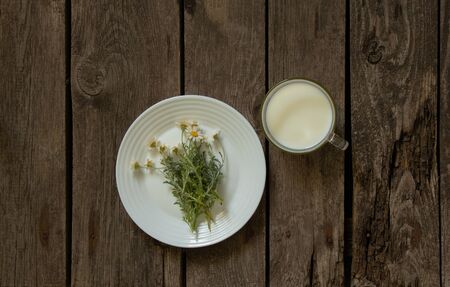 cup of milk and chamomile flower on a plate on a tableの写真素材