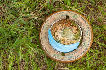 planet globe and medical mask lies on the grass on the street during a pandemicの写真素材