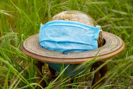 planet globe and medical mask lies on the grass on the street during a pandemicの写真素材
