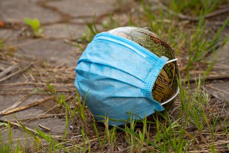 planet globe and medical mask lies on the grass on the street during a pandemicの写真素材